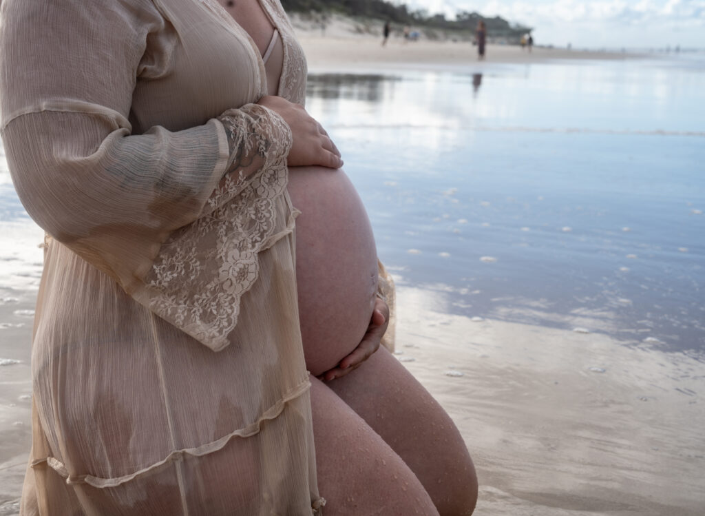 Pregnant woman holding her baby bump on the beach.